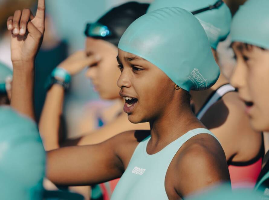 A young girl wearing a swim cap stands among a group of people, all engaged in a swimming activity.