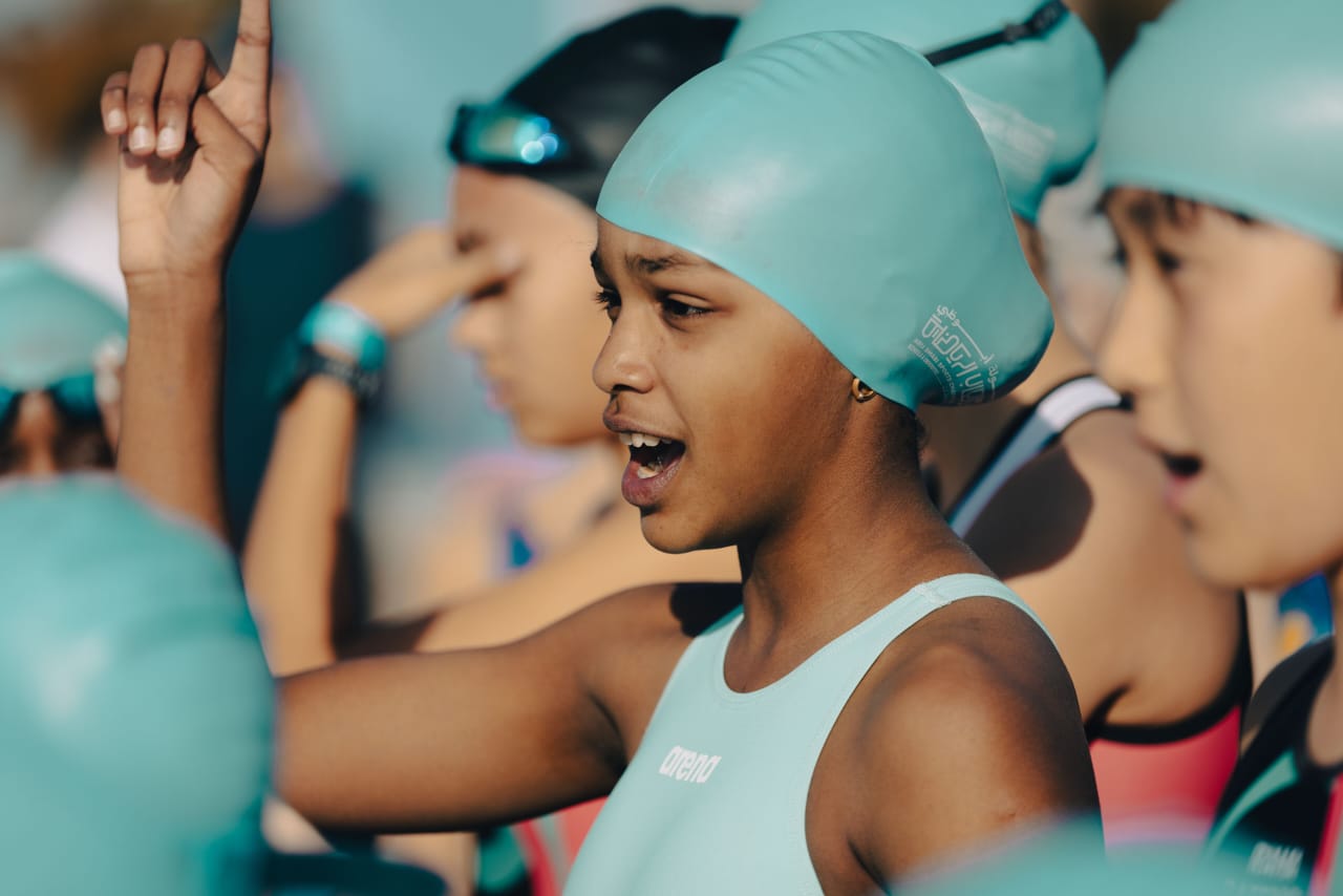 A young girl wearing a swim cap stands among a group of people, all engaged in a swimming activity.